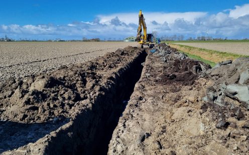 A trench for a field drainage system being dug by a large yellow digger