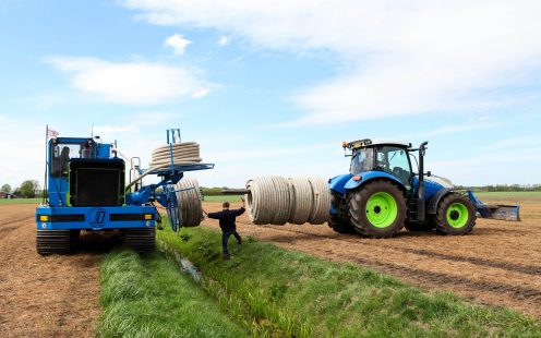 Coils of field drainage pipes being transferred from a tractor to the pipe laying machine