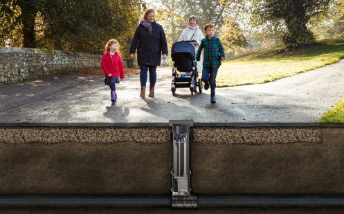 A photo with two women and three children, one in a stroller, walking in the park. The Smart Probe system is shown below the asphalt.