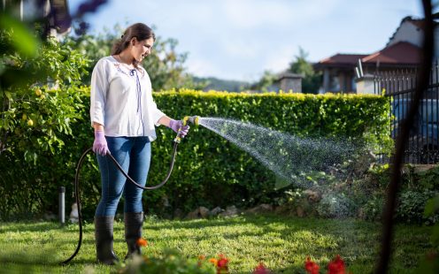 Young Latino woman in full Length holding watering garden with water hose.