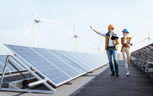 View on the rooftop solar power plant with two engineers walking and examining photovoltaic panels. Concept of alternative energy and its service