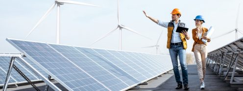 View on the rooftop solar power plant with two engineers walking and examining photovoltaic panels. Concept of alternative energy and its service