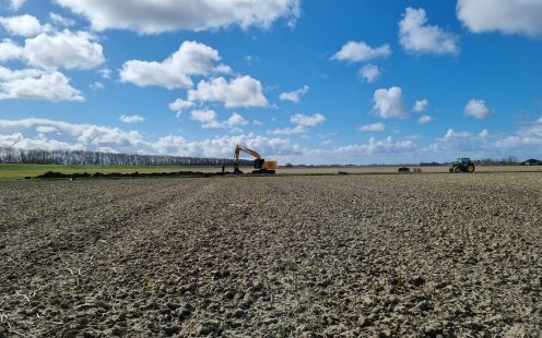 A wide-angle view of a freshly ploughed field with an excavator working in the background | Pipelife