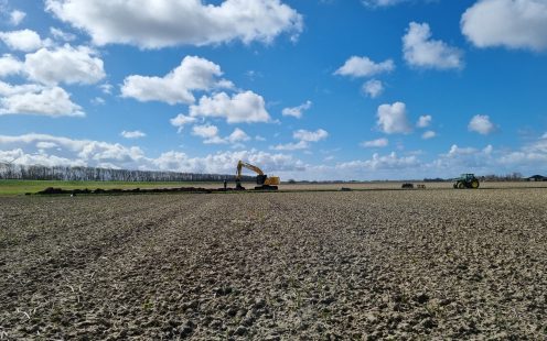 A wide-angle view of a freshly ploughed field with an excavator working in the background | Pipelife