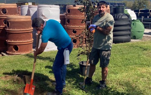 Two employees are planting a young apple tree at the Botevgrad plant with several Pipelife's products visible at the background | Pipelife