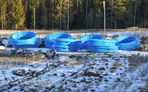 Six rolls of Pipelife Robust pipes lying on a snow-clad field next to a forest | Pipelife