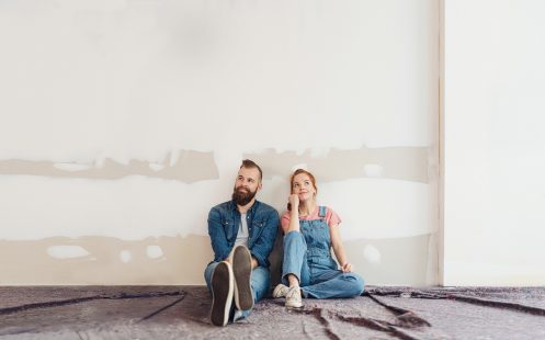 Two young people sitting on the floor in a room undergoing renovation.