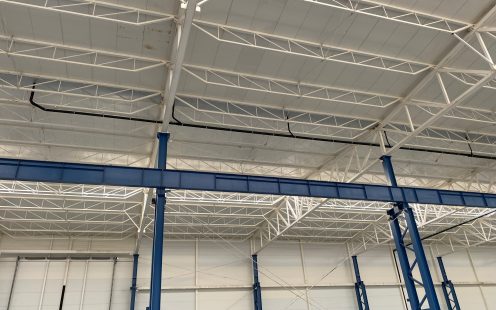 A black, horizontal drainpipe installed across the warehouse ceiling.