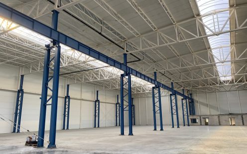 A large, empty, newly built warehouse with black siphonic drainage pipes installed near the roof