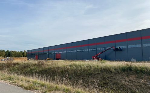 A recently built warehouse from outside with a red crane next to it and some installers working.