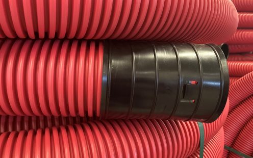 A close-up of red, coiled, corrugated cable protection pipe.
