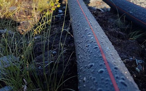 Two black PE-100 RC cable protection pipes laying on the ground and covered in dew.