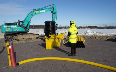 Two electricians standing near an excavator and several yellow, corrugated PE cable ducts.