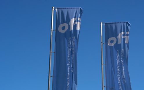 Two light blue flags with the OFI logo photographed against the sky.
