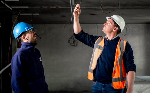 Two installers examine electrical cables hanging from the ceiling.